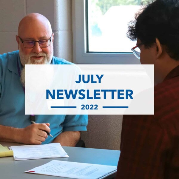 Two people sit across a table from each other, discussing documents. Overlaid text reads “JULY NEWSLETTER 2022.” Sunlight comes through a window in the background.