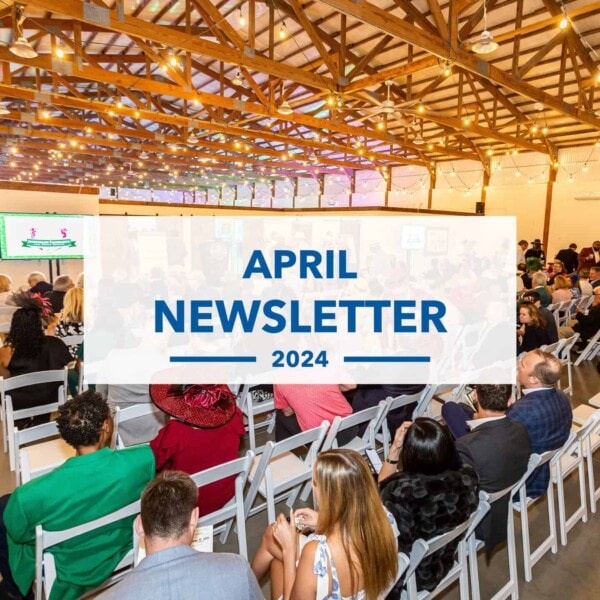 A large group of people seated in rows at an indoor event with wooden beams, facing a presentation screen. Overlaid text reads April Newsletter 2024.