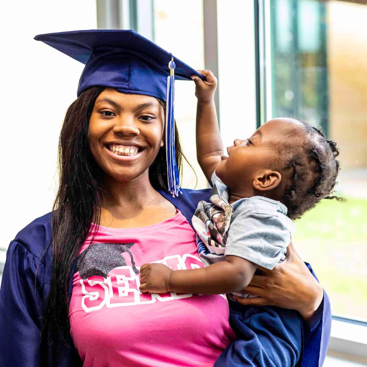 Smiling young woman with a graduation toga holding a child